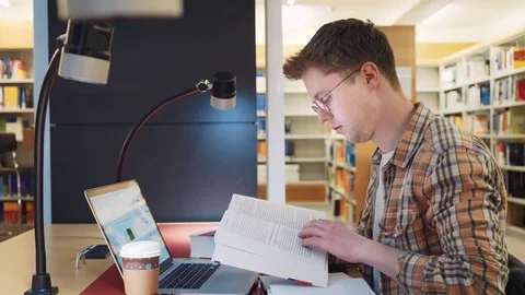 A student in the library prepares for exams typing on a computer and writes in a Vídeos de archivo 79903658