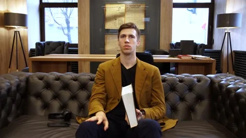 A student in the library reads a huge book on a large leather sofa 스톡 동영상 155963342