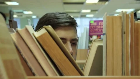 Student in the library view through the shelves with books Stock Footage 155962844