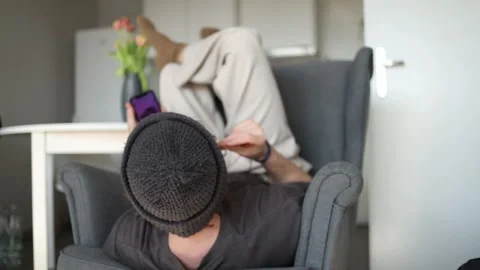 A student lies upside down in a chair, focused on his phone, scrolling through s Stock Footage 302634935
