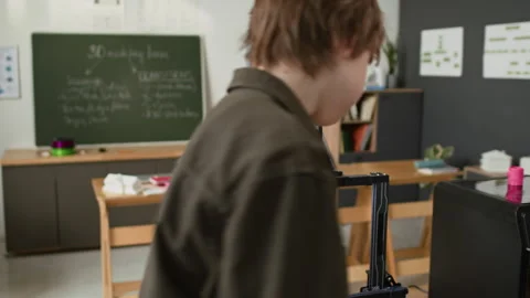 Student Loading Spool of Gray Filament Into Open-Frame 3D Printer in Class Stockbeeldmateriaal 335690568