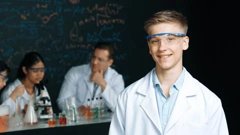 Student looking at camera while diverse group doing experiment. Edification. 스톡 사진