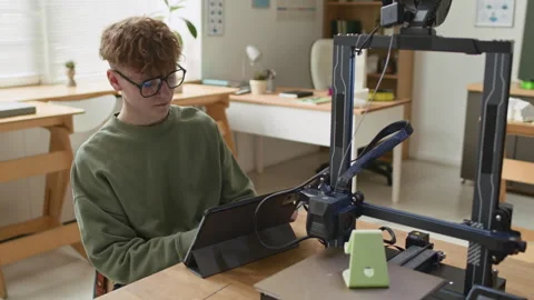 Student Looking at Digital Tablet Connected to 3D Printer in Classroom Stockbeeldmateriaal 335689094