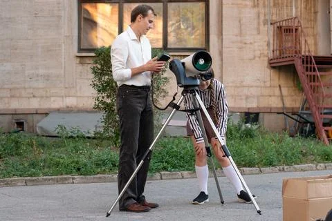 Student looking through telescope while teacher supervises outdoors 写真素材