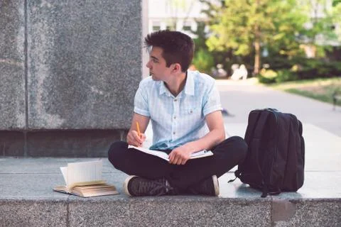 Student making the notes sitting on a monument outside of university Stock Photos