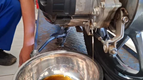 Student Mechanic Draining Scooter Engine Oil into Metal Container Stock Footage 328909736