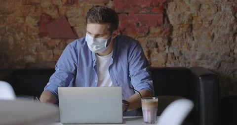 Student with medical mask using laptop and sitting it coffee shop. Handsome man Stock Footage 166301771