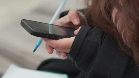 Student multitasks outdoors. Student writes notes while scrolling messages Stock Footage 331360323