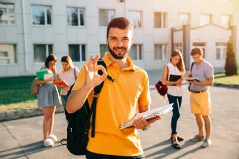 Student with note-books and backpack smiling and showing okay while standing  Stock Photos