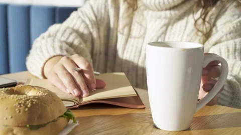 Student in oversize sweater writes notes near cup and burger Stock Footage 151952802