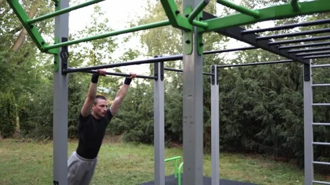 Student performs explosive muscle up on horizontal bar in outdoor gym surrounded Stock Footage 316701713