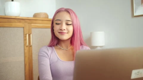 Student with pink hair uses a computer to study online, Stockbeeldmateriaal 243813997