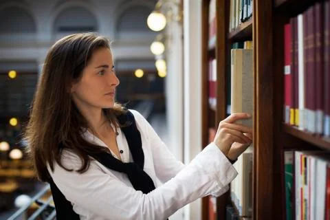 Student pulling out book from bookshelf Stock Photos