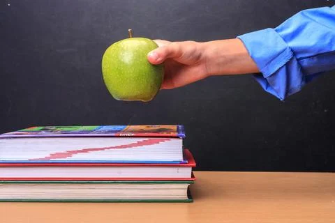 Student puts apple on desk. Stock Photos