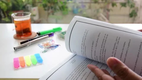 The student quickly turns the pages of a large book lying on a white desk, Stock Footage 137145664