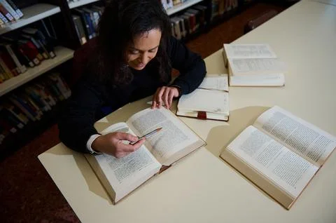 Student reading books in a library environment while studying and taking note Stock Photos