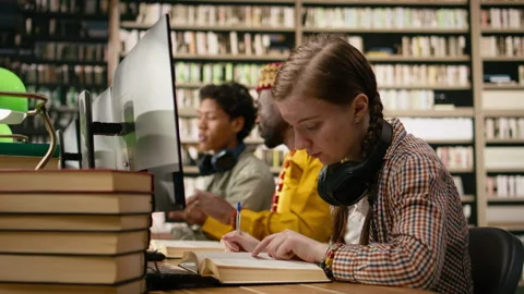 Student reading open book closely at wooden library table Stock Footage 337228988
