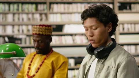 Student reading open book at library desk near chatbot on computer screen Stock Footage 337231597