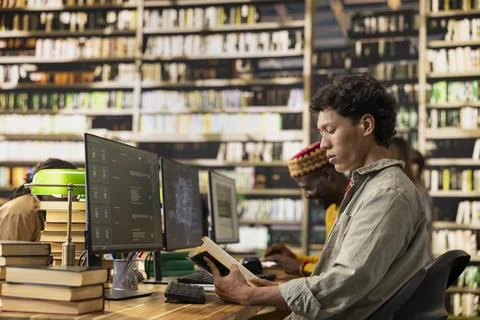 Student reading open book at library desk near chatbot on computer screen 写真素材