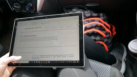 Student reading physics ebook swiping on a tablet in a car zooming in and out Stock Footage 95964520