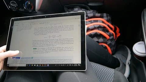 Student reading physics ebook swiping on a touch screen computer in a car Stock Footage 95964851