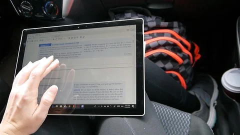 Student reading physics ebook on a touchscreen computer sitting in a car Stock Footage 95964595