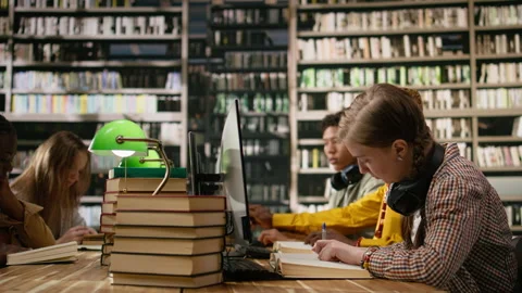 Student reading textbook and browsing computer at library study desk Stock Footage 337228926