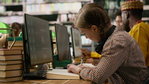 Student reading textbook and browsing computer at library study desk Stock Footage 337231189