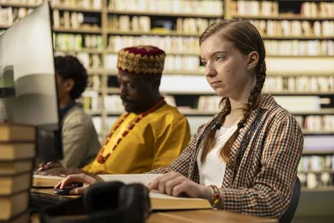 Student reading textbook and browsing computer at library study desk Stock Photos