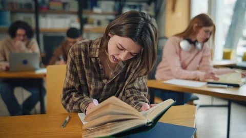 Student reads a book in a library while classmates work at desks during study ti Stock Footage 337163603