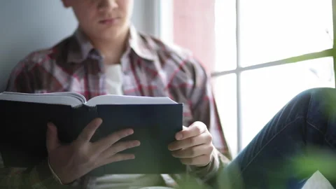 A student reads a book while sitting on a windowsill. A young man spends his Stock Footage 131091249