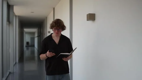 Student reads notes while walking through a university hallway Stock Footage 337851735