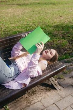 Student relaxing on a bench while reading a book outdoors on a sunny day Foto stock