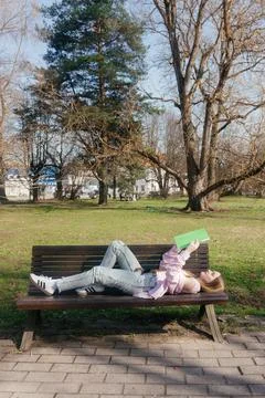Student relaxing on a bench while reading a book outdoors on a sunny day Foto stock