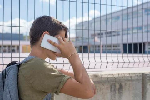 Student resting outside a school and playing with a mobile phone Stock Photos