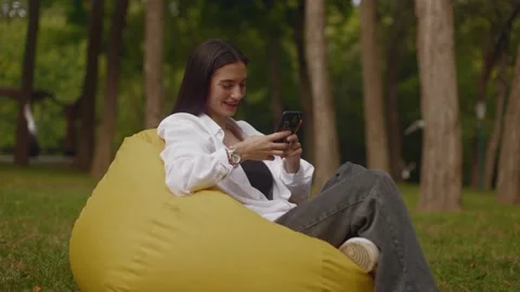 Student resting in the shade of a tree in the park sitting on a bean bag chair Stock Footage 235930838