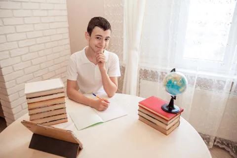 Student sits at the table at the bookside with a pen in his hands. A tired te Stock Photos