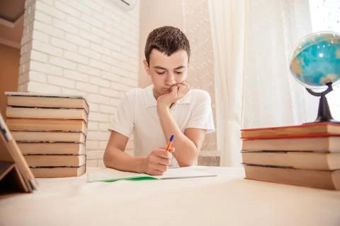 Student sits at the table at the bookside with a pen in his hands. A tired te Foto stock