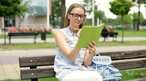 Student sitting on the bench and doing homework in her notebook Stock Footage 67378684