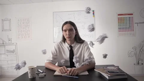 Student sitting at a desk in class is hit in the face with crumpled papers Stock-Footage 264511516