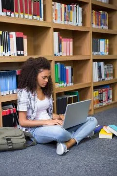 Student sitting on floor in library using laptop 스톡 사진