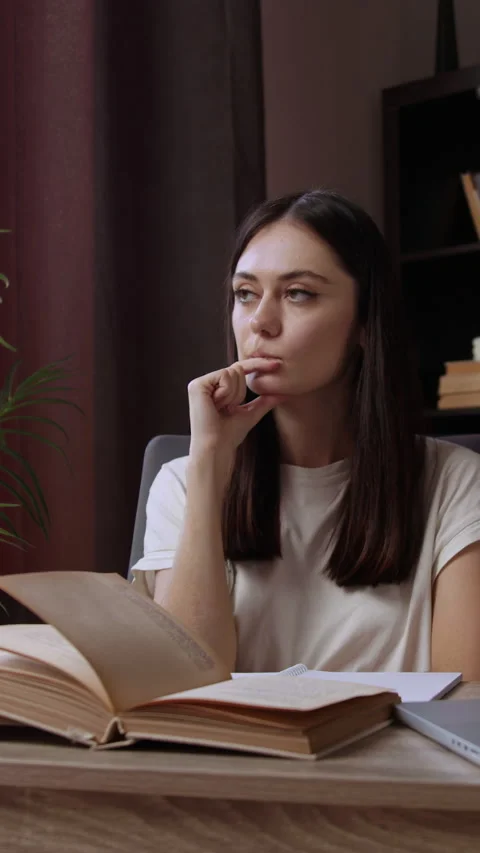 Student sitting at an office table with a thoughtful face is analyzing several Stock Footage 305409336