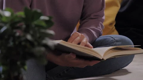 Student sitting on a sofa, reading a book, turning pages Stock Footage 133465559