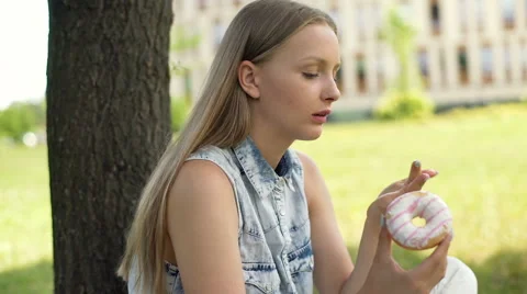 Student sitting under the tree and eating donut during break 動画素材 67369858