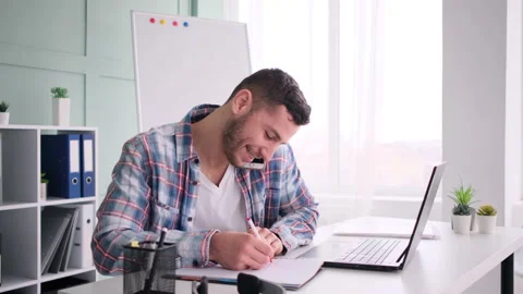 Student sitting at working place, working on laptop computer, talking phone Stockbeeldmateriaal 171545383