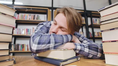 Student sleeping on books while studying in a library during the afternoon hours Stock Footage 318090518