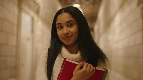 Student smiles in corridor while holding a red book during school day Stock Footage 312769036