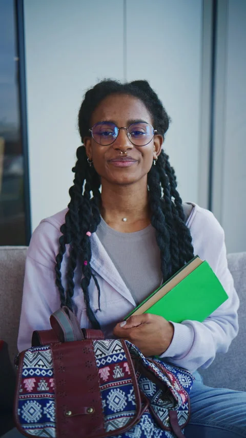 Student smiling while sitting on a couch in a study area with books and a bag in Stock Footage 339558994