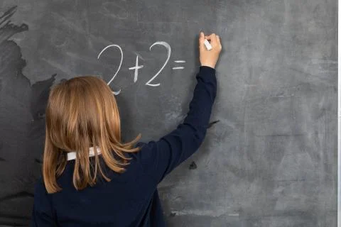 The student solves a math problem standing at the blackboard in her classroom Stock Photos