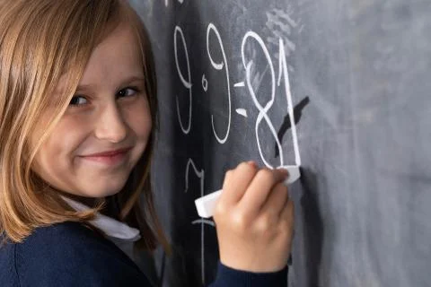 The student solves a math problem standing at the blackboard in her classroom Stock Photos